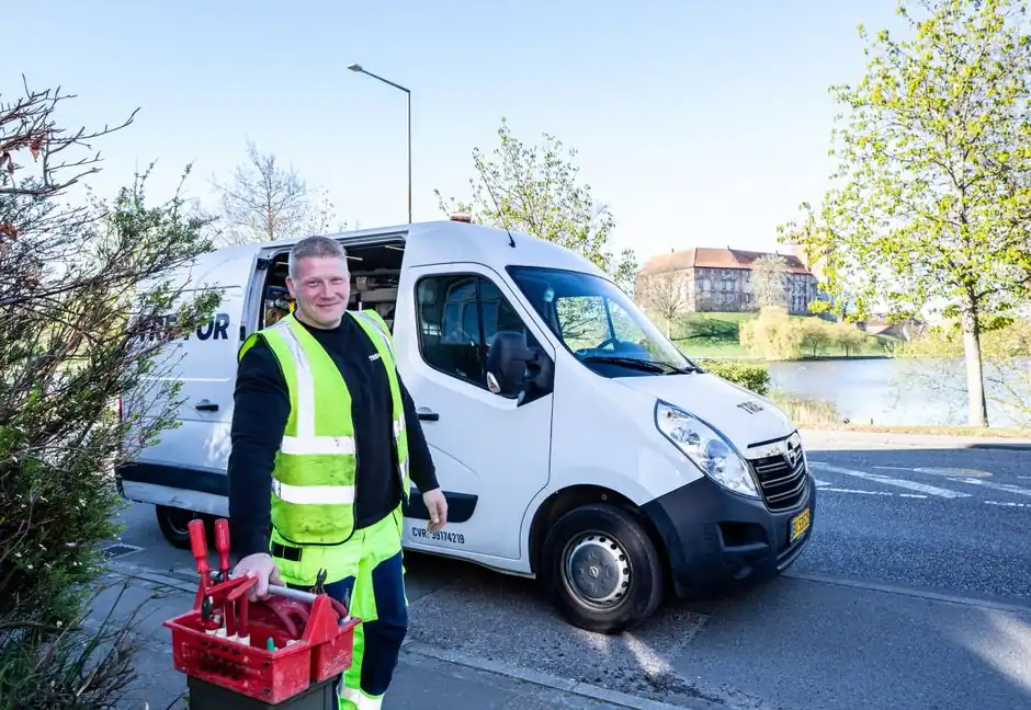 Smiling worker in reflective vest stands by a van holding tools.